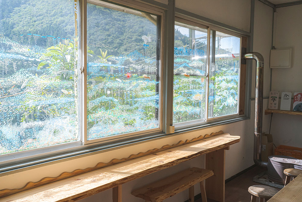 写真：窓際のカウンター席。窓にはイラストが描いてあり、窓の外の山の景色と混ざり合っている